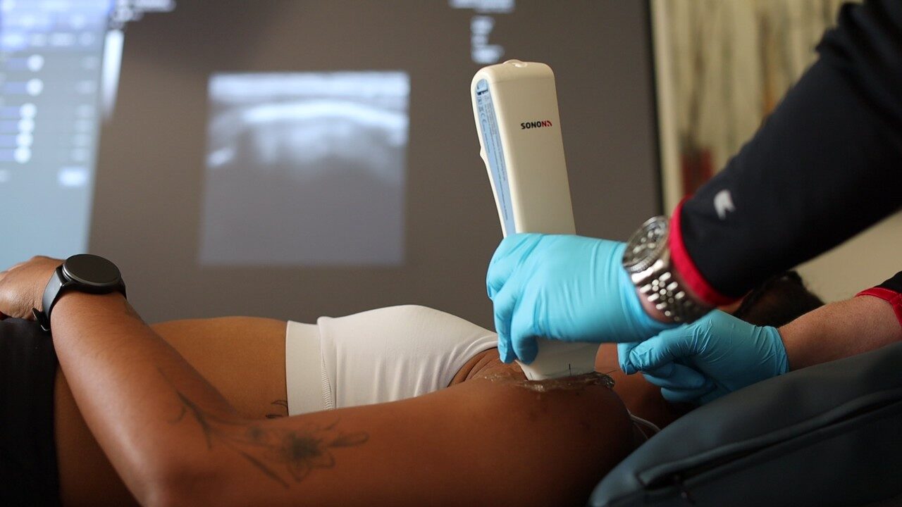 A close-up of a clinician using a handheld ultrasound probe to guide a regenerative treatment