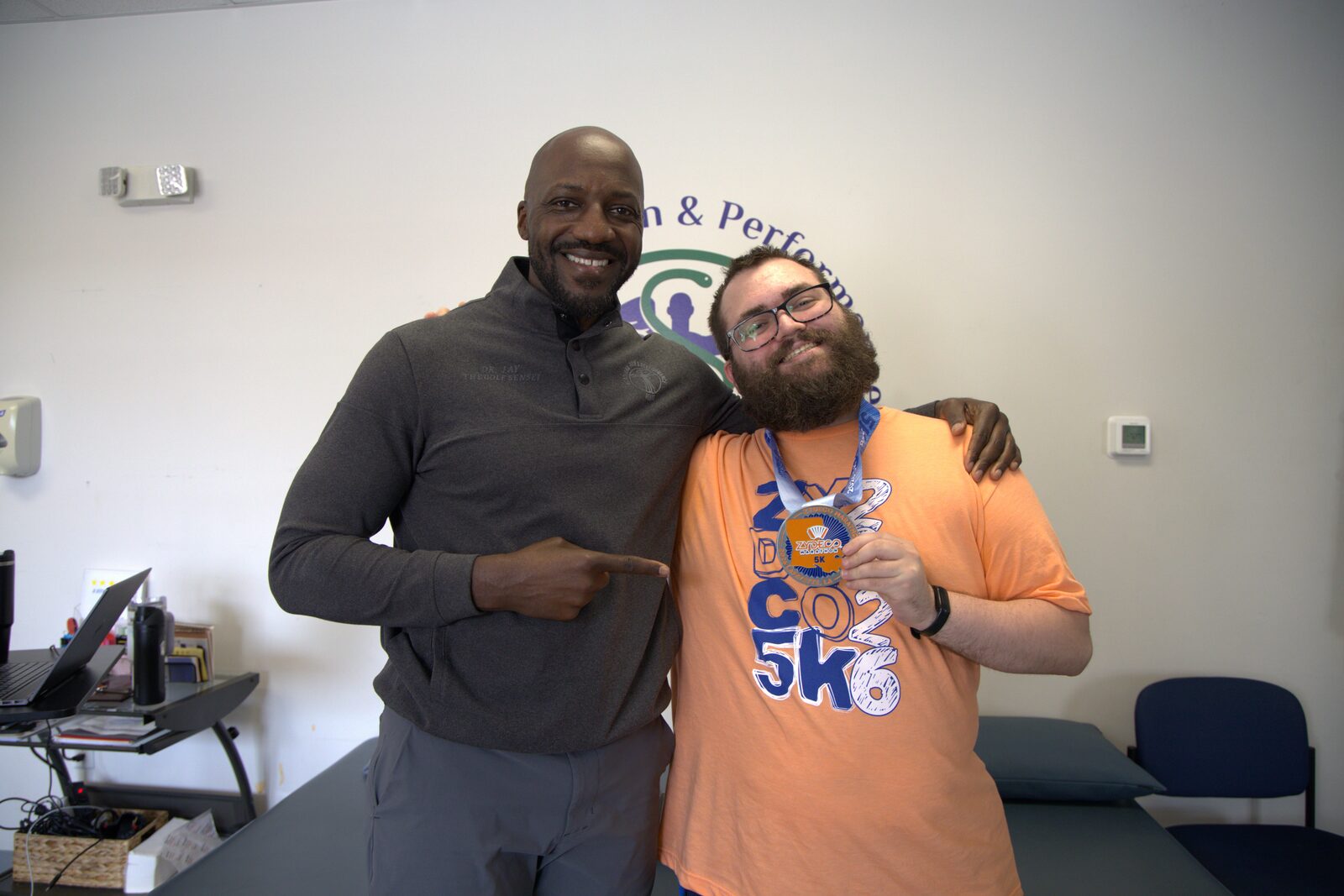 A patient celebrating a 5K medal with his doctor at Acadiana Pain & Performance Rehab