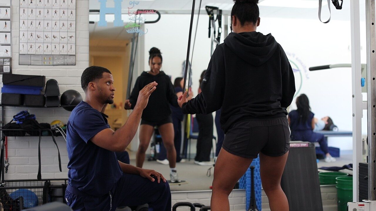 A therapist coaching an athlete through a cable resistance exercise in the gym